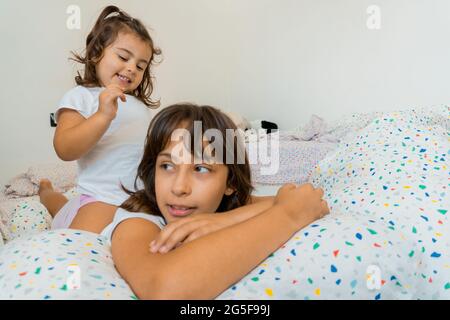 Due ragazze caucasiche, di due e nove anni, si divertono insieme sui loro letti della camera da letto, giocando e parlando. Foto Stock