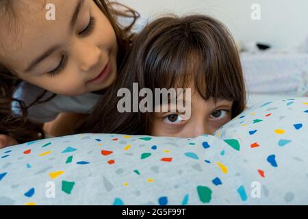 Due ragazze caucasiche, di due e nove anni, si divertono insieme sui loro letti della camera da letto, giocando e parlando. Foto Stock