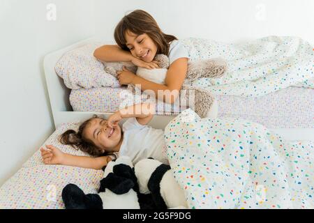 Due ragazze caucasiche, di due e nove anni, si divertono insieme sui loro letti della camera da letto, giocando e parlando. Foto Stock