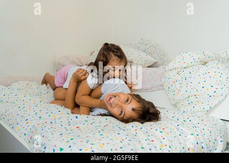 Due ragazze caucasiche, di due e nove anni, si divertono insieme sui loro letti della camera da letto, giocando e parlando. Foto Stock