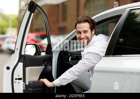 Grande offerta, uomo d'affari che compra l'automobile seduto nel sedile del conducente, auto di prova nello showroom della concessionaria. Sorridente millennesimo bel driver ragazzo con stoppia o Foto Stock