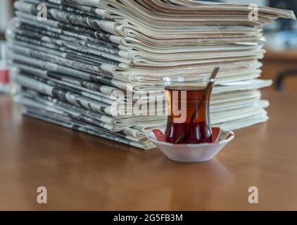 Un bicchiere di tè turco su un tavolo di legno con un mucchio di giornali Foto Stock