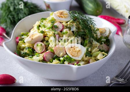 Insalata con cavolo cinese, cetriolo, rafano, cipolle verdi e uova di quaglia in un piatto bianco su sfondo grigio. Primo piano Foto Stock