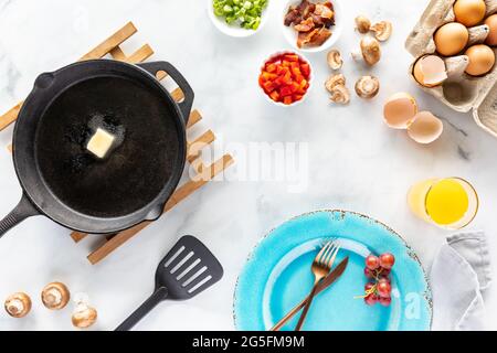 Vista dall'alto di tutti gli ingredienti utilizzati per preparare una frittata fatta in casa e una padella con burro fuso. Foto Stock