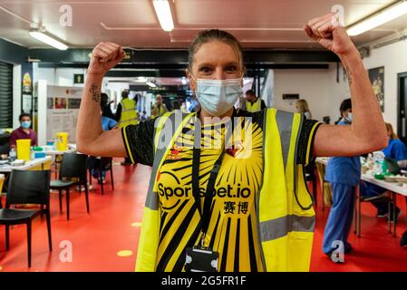 Watford, Regno Unito. 27 giugno 2021. Un membro dello staff che indossa una maglietta da club si pone in una clinica pop-up di vaccinazione di massa al Vicarage Road Stadium del Watford FC come parte della campagna "Grab a jab". Il NHS sta inoltre promuovendo un certo numero di ambulatori di walk-in questo fine settimana attraverso la capitale per cercare di aumentare il numero di oltre 18 che ricevono un jab come casi della variante di Delta sono riportati per essere in aumento. Credit: Stephen Chung / Alamy Live News Foto Stock