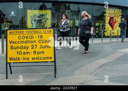 Watford, Regno Unito. 27 giugno 2021. La gente passa un cartello fuori da una clinica pop-up di vaccinazione di massa al Vicarage Road Stadium del Watford FC come parte della campagna "Grab a jab". Il NHS sta inoltre promuovendo un certo numero di ambulatori di walk-in questo fine settimana attraverso la capitale per cercare di aumentare il numero di oltre 18 che ricevono un jab come casi della variante di Delta sono riportati per essere in aumento. Credit: Stephen Chung / Alamy Live News Foto Stock