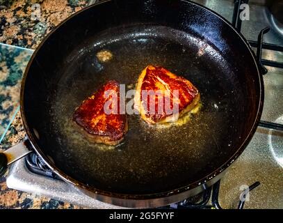 Il secondo lato di due piccole bistecche di filetto di manzo fritte in olio d'oliva in una padella antiaderente su un piano cottura a gas Foto Stock