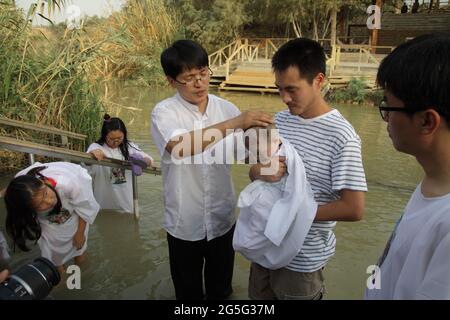 Il pastore coreano protestante ha la mano sulla testa di un bambino tenuto dal padre, benedicendolo prima di battezzarlo nel fiume Giordano, dove Cristo fu battezzato Foto Stock