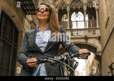 La donna d'affari conduce in bicicletta a mano a casa per lavorare nella bella città vecchia del centro Foto Stock