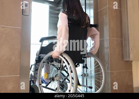 Donna disabili in sedia a rotelle che entra nella vista posteriore dell'ascensore Foto Stock