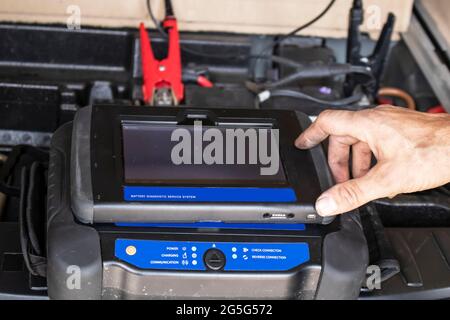 Riparare la mano sporca prepararsi allo schermo del computer touch sull'unità diagnostica mobile polverosa caricando la batteria dell'auto con clip sfocate sul termin della batteria Foto Stock