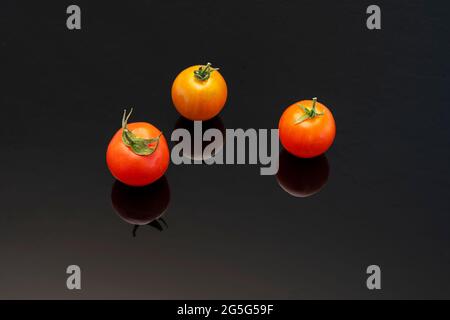 Tre pomodori ciliegini con riflessi su sfondo nero. Foto Stock