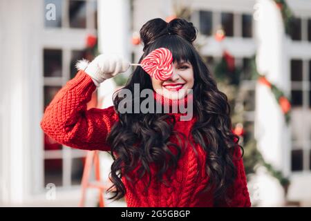 Carina donna dai capelli scuri in pullover rosso con lollipop Foto Stock