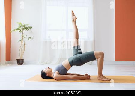 Giovane donna in leggings e T-shirt corta, pratica yoga, facendo dvipada pithasana con gamba estesa verso l'alto, mezzo ponte posa Foto Stock