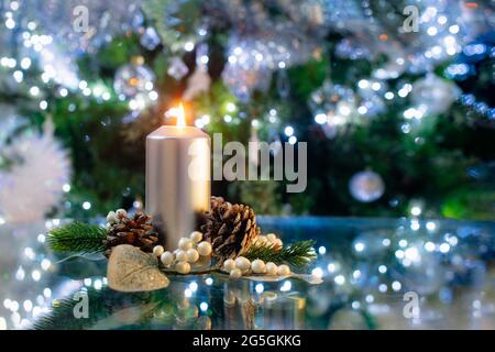 Candela in argento con decorazione di natale di abete e coni, di fronte ad un albero di Natale verde con luci bokeh, fuoco selettivo, copia Foto Stock