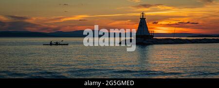 I kayak si avvicinano al faro del lago Champlain Breakwater con un uccello di mare arroccato sulla cima al tramonto Foto Stock