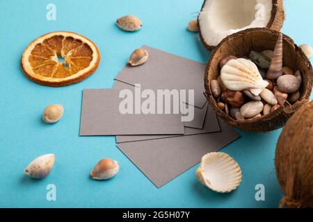 Biglietto da visita di carta grigia con cocco e conchiglie su sfondo blu pastello. Vista laterale, spazio di copia. Tropicale, cibo sano, vacanza, conce vacanze Foto Stock