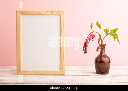 Cornice in legno con dicentra rosa, cuore rotto in vaso in ceramica su sfondo rosa pastello. Vista laterale, copia spazio, mockup, dima, primavera, estate minim Foto Stock