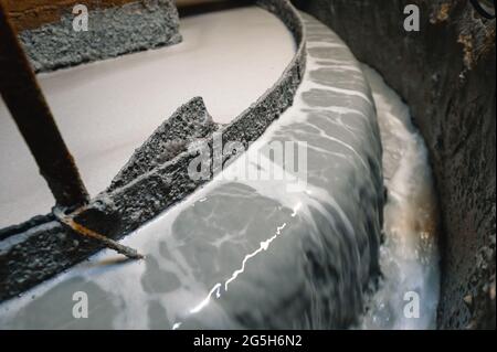 Macchina di flottazione. Un flusso di liquido grigio sporco scorre verso il basso dal bordo di separazione del bagno Foto Stock