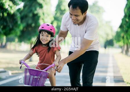 Padre insegnante figlia di guidare in bicicletta nel parco Foto Stock