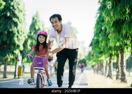 Padre insegnante figlia di guidare in bicicletta nel parco Foto Stock