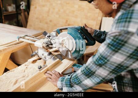 Immagine ravvicinata del falegname che taglia la tavola di legno con sega circolare nella sua officina Foto Stock