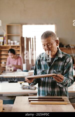 Carpentiere concentrato che controlla la qualità dei pezzi di legno di noce e acero fusi insieme Foto Stock