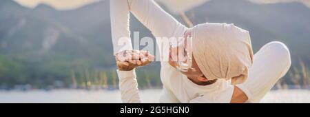 BANNER, LUNGA FORMATO Kundalini yoga donna in abiti bianchi e turbani pratica yoga kundalini sullo sfondo del mare, montagne e tramonto Foto Stock