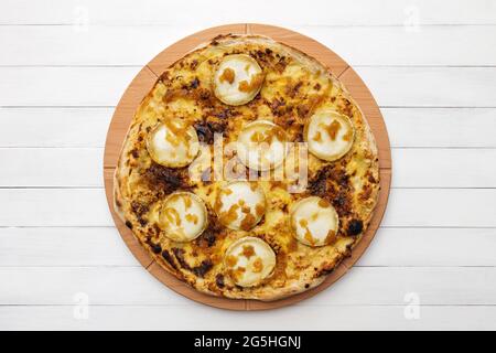 Pizza rotonda intera con formaggio di capra e cipolla caramellata su piatto di legno. Vista dall'alto sullo sfondo della lavagna bianca Foto Stock