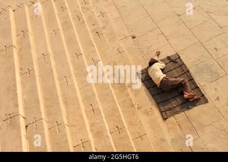 VARANASI, INDIA - 03 FEBBRAIO 2021: Uomo non identificato che dorme sulla piattaforma di un ghat presso il fiume Gange a Varanasi, India Foto Stock