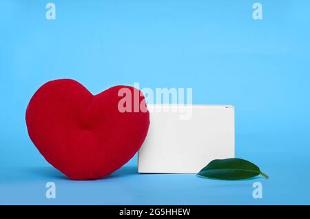 Mock-up. Un cuore peluche e una foglia di ficus su uno sfondo blu Foto Stock