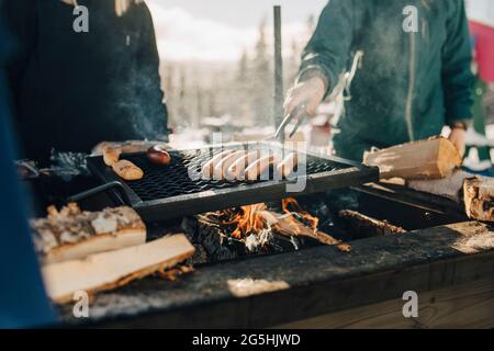Sezione centrale di amici che preparano le salsicce sulla griglia del barbecue Foto Stock