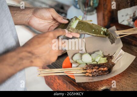 preparazione di sate ayam servita con torta di riso o lontong con salsa di arachidi su carta alimentare Foto Stock