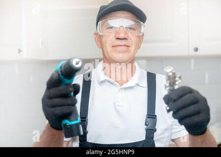 L'uomo lavoratore in uniforme installa i raccordi che assemblano i mobili in cucina. Foto Stock