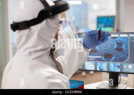 Scienziato che analizza il campione di sangue in vaccutainer vestito con dpi. Team medico che esamina l'evoluzione dei vaccini in laboratorio medico utilizzando strumenti di alta tecnologia e chimica per la ricerca scientifica Foto Stock