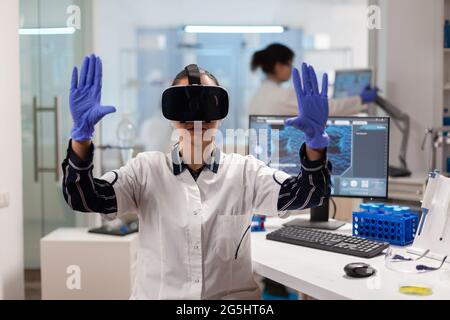 Medico biochemista che sperimenta la realtà virtuale indossando cuffie durante l'esperimento del vaccino. Team di ricercatori che lavorano con apparecchiature, futuro, medicina, assistenza sanitaria, professionisti, visione, simulatore. Foto Stock