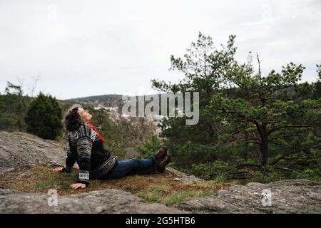 Vista laterale di una donna che si siede sulla roccia nella foresta Foto Stock