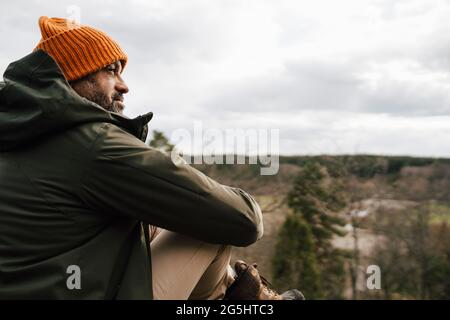 Uomo maturo che guarda via seduto sulla montagna contro il cielo Foto Stock