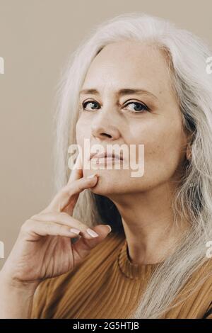 Ritratto di donna matura sicura con mano su sedia su sfondo beige Foto Stock