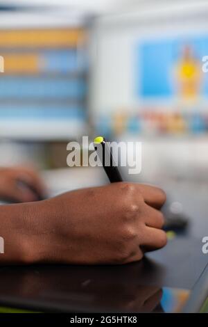 Primo piano di un ritocco fotografico africano che tiene la penna stilo per modificare la foto del cliente utilizzando il computer con due display. Black woman editor ritocco risorse disegno su tavoletta grafica in ufficio agenzia creativa Foto Stock