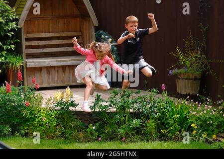 Sorella e fratello saltano sopra un letto fiorito in un giardino Foto Stock