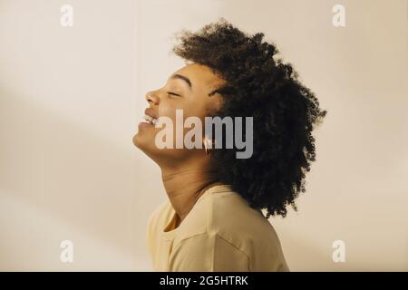 Vista laterale della donna dai capelli ricci con gli occhi chiusi contro la parete beige Foto Stock