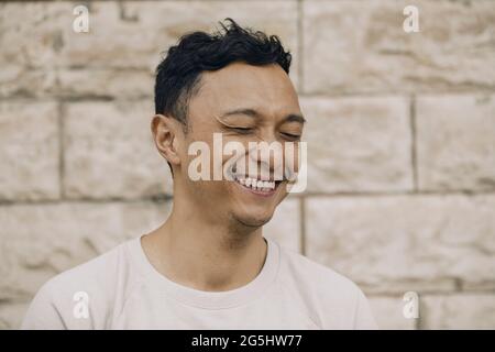 Uomo allegro con occhi chiusi contro parete beige Foto Stock