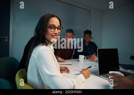 Ritratto di una giovane donna sorridente che guarda la fotocamera mentre lavora sul posto di lavoro Foto Stock