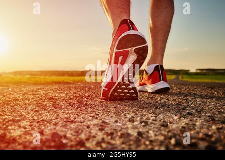 Piedi del corridore maschile sulla strada al tramonto, primo piano. Sneaker sportive per jogging. Concetto di forma fisica e stile di vita sano Foto Stock