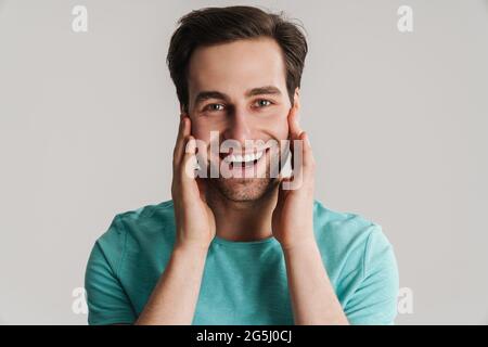 Gioioso bel ragazzo sorridente e toccante il suo volto isolato su sfondo bianco Foto Stock