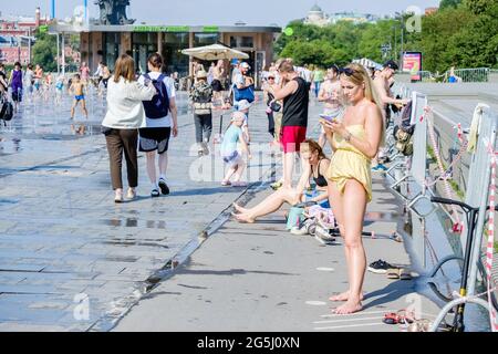 Mosca. Russia. 26 giugno 2021. Donne e uomini prendere il sole in una calda giornata estiva. Sullo sfondo, molti bambini e adulti si bagnano nella fontana della città. Foto Stock