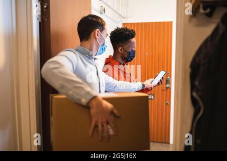 Cliente maschile che riceve il pacco da un giovane addetto alla consegna durante il COVID-19 Foto Stock