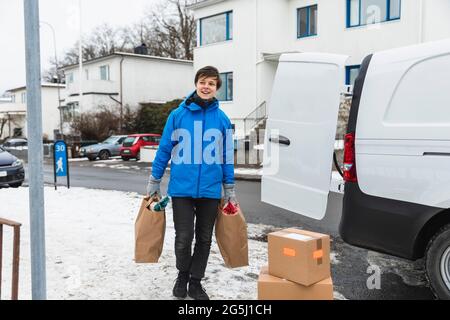 Sorridente donna di servizio essenziale che consegna sacchetti di carta durante l'inverno Foto Stock