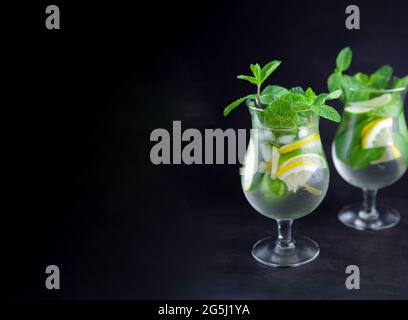Mojito su sfondo nero. Bevande analcoliche estive con spazio per fotocopie. Limone, lime, menta, ghiaccio, acqua. Menu bar, due bicchieri a nebbia con spazio per il testo. Bevanda estiva fredda. Foto Stock